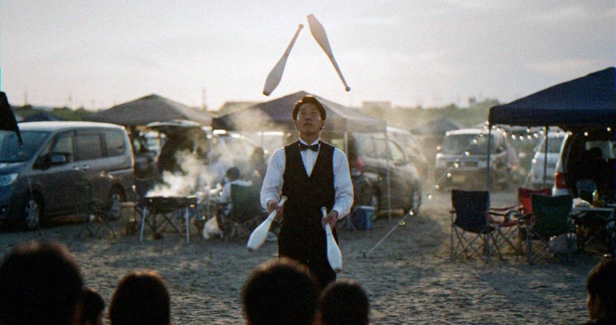 車が並ぶVIPエリアで、BBQを囲む来場者の前でジャグリングを披露するプロのパフォーマー